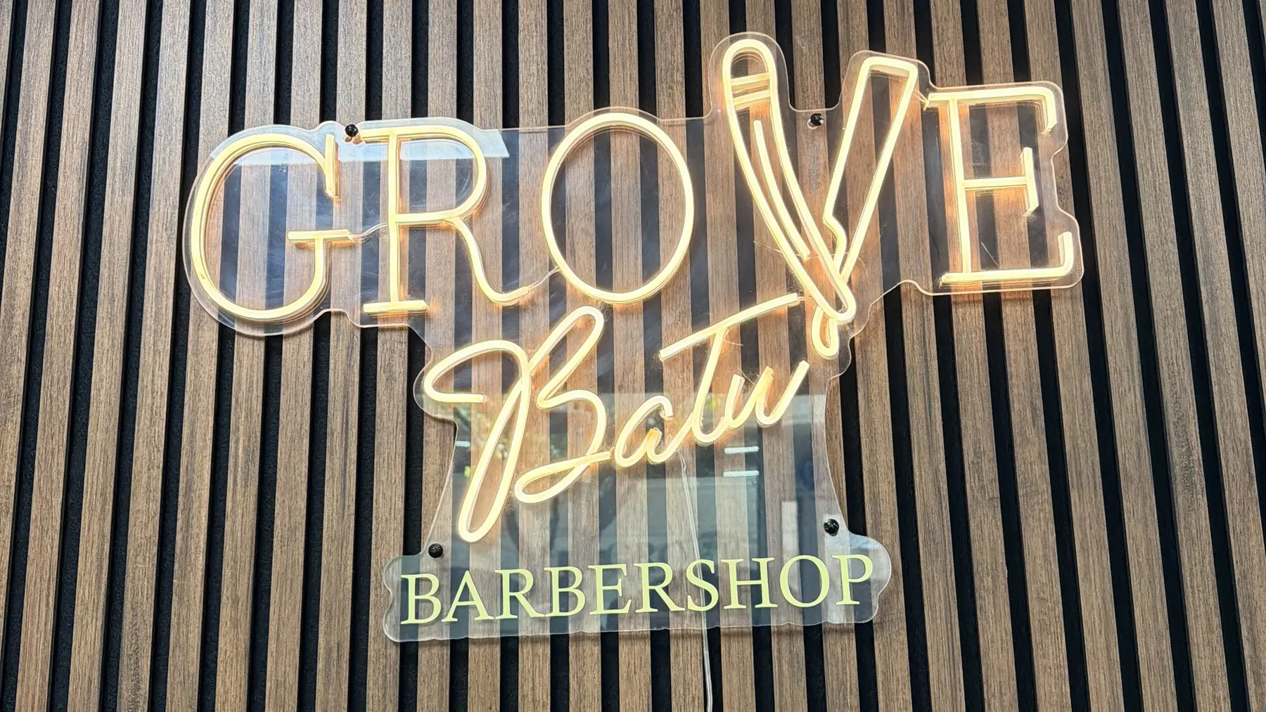 The Grove Batu Barbershop neon sign lit on the wood slat wall inside the shop